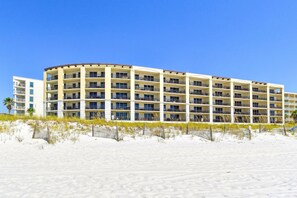 Un hotel de varios pisos con balcones, situado en una playa de arena.