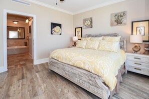 A bedroom with a large bed, wooden flooring, and artwork on the walls. - Coastal, upgraded, & luxurious w/beach and pool views! ✨ (Fort Walton Beach)