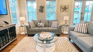A living room with a grey sofa, two side tables with lamps, a glass coffee table, and a TV on the wall. - Crosswinds Beach House - 4BR home by 30A, bikes included! (Santa Rosa Beach)