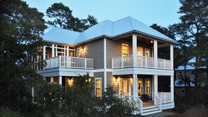 A two-story house with a balcony, a covered porch, and a well-lit entrance. - Crosswinds Beach House - 4BR home by 30A, bikes included! (Santa Rosa Beach)