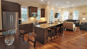 A modern kitchen with a central island, dark wooden cabinets, stainless steel appliances, and a dining area with a wooden table and chairs. - Crosswinds Beach House - 4BR home by 30A, bikes included! (Santa Rosa Beach)