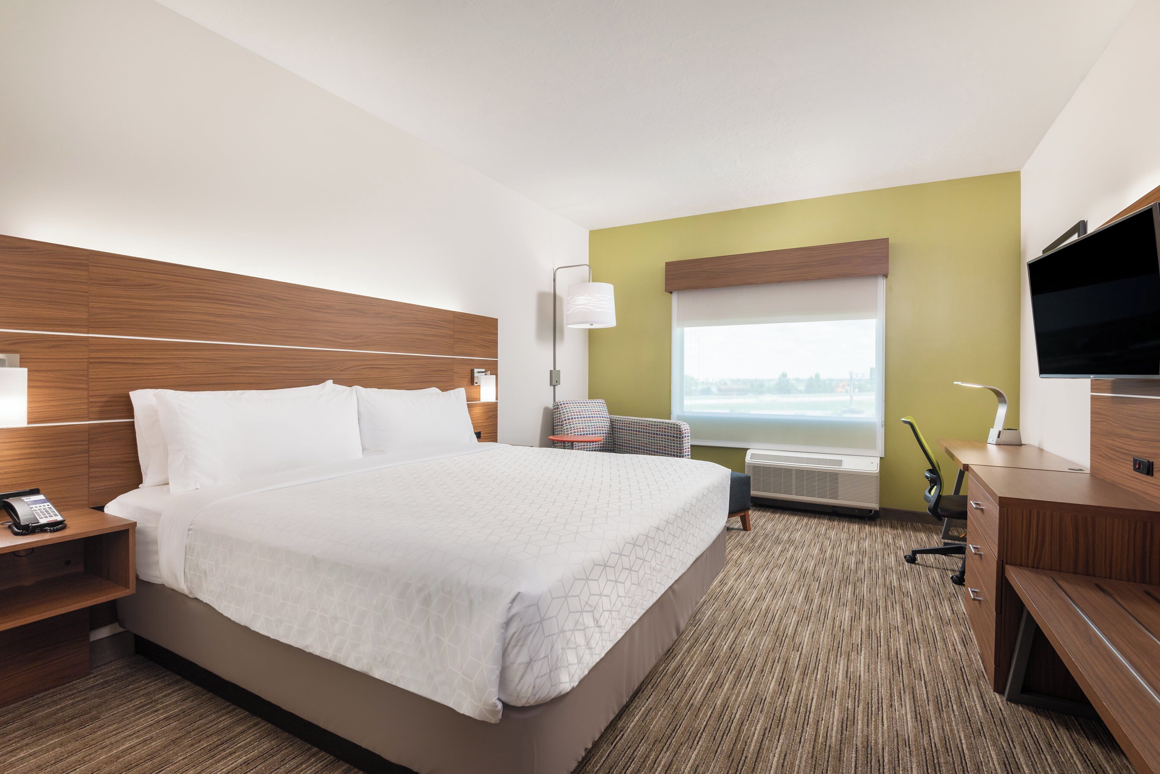 A hotel room with a large bed, bedside tables, a desk with a chair, a flat-screen TV, and a window with a view.