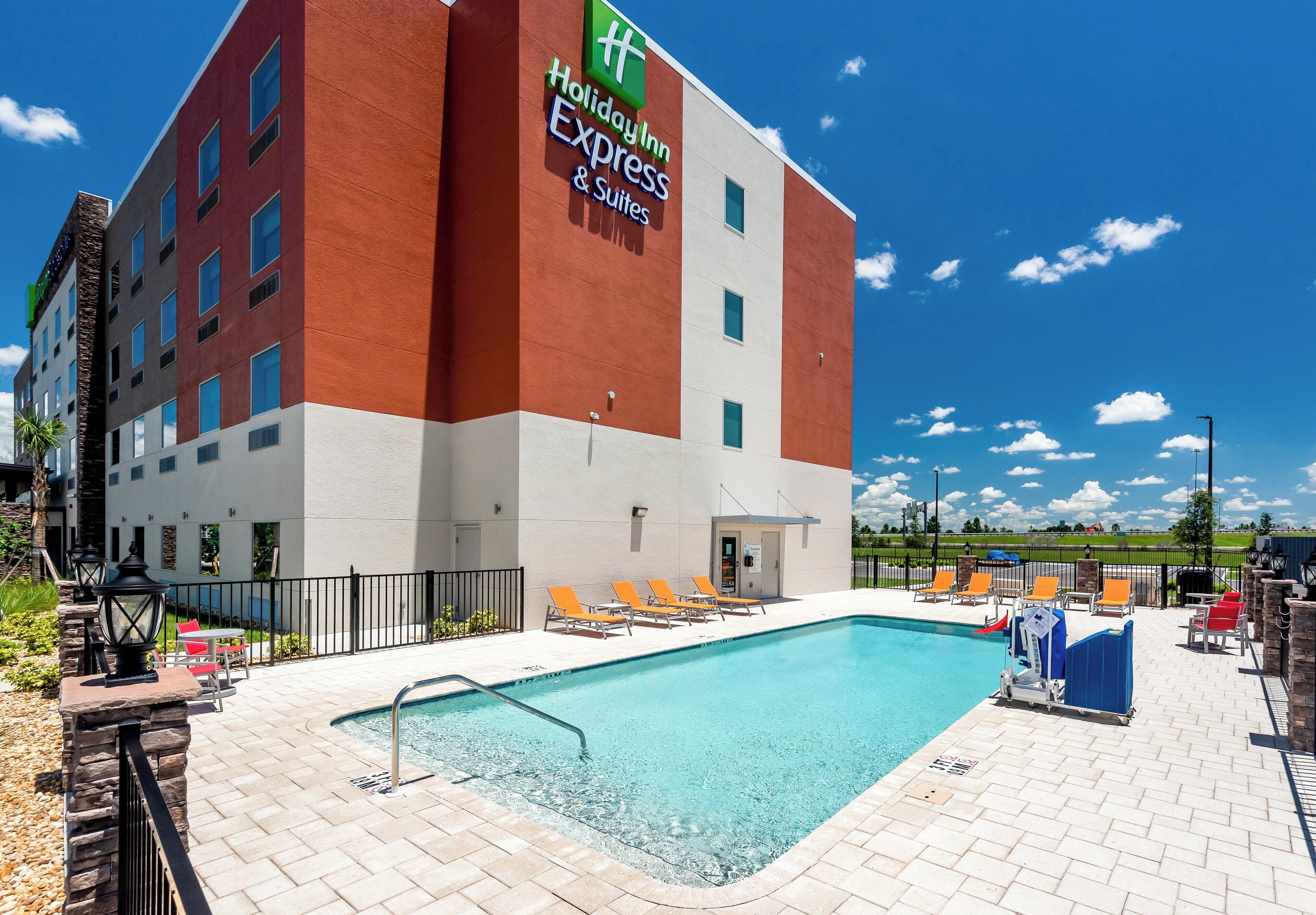 Edificio de Holiday Inn Express con piscina, mobiliario exterior y cielo despejado.
