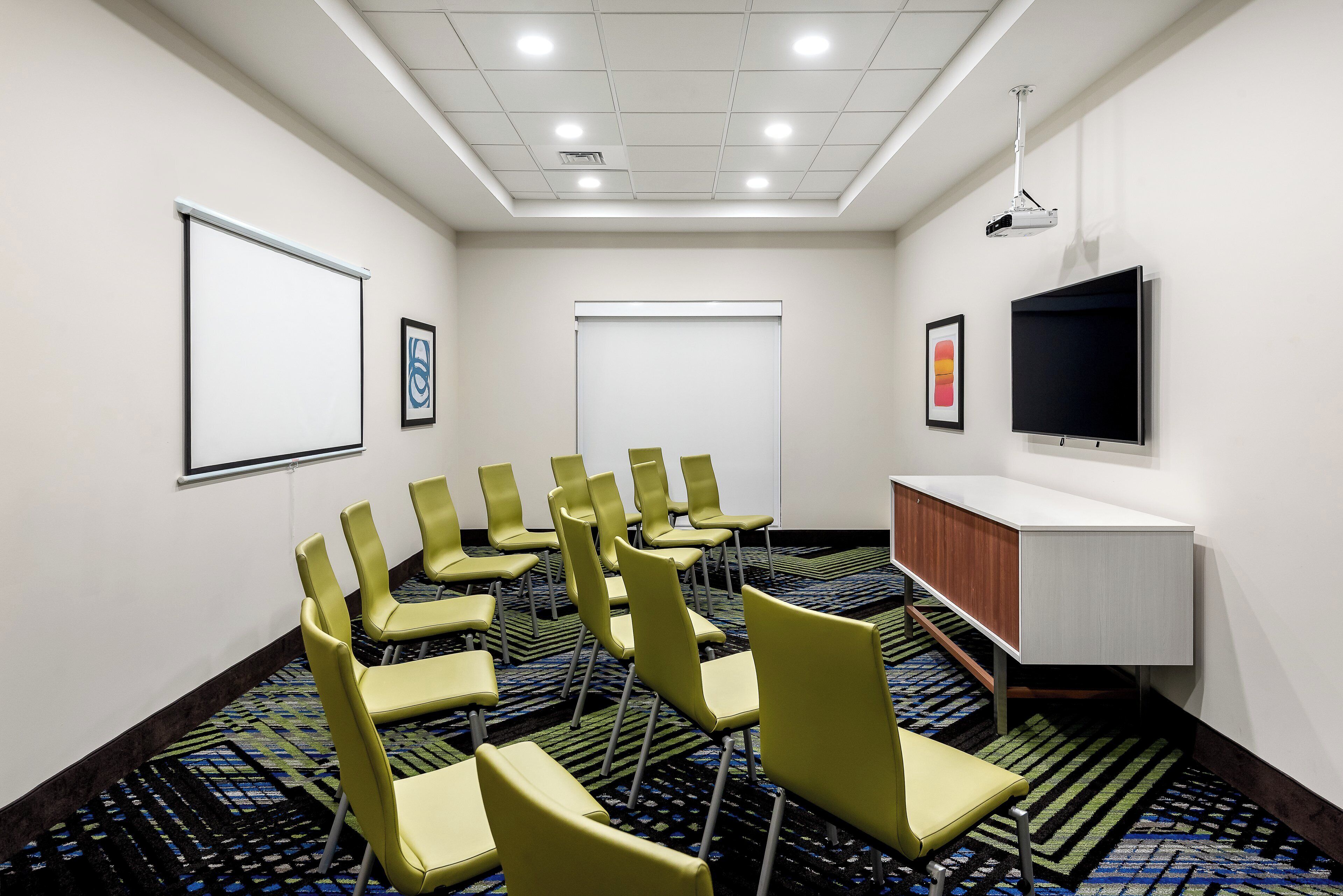 A conference room with a projector screen, a flat-screen TV, and a carpeted floor.
