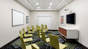 A conference room with a projector screen, a flat-screen TV, and a carpeted floor.