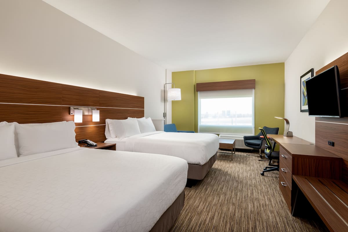 A hotel room with two beds, a desk, a chair, a TV, and a window with a city view.