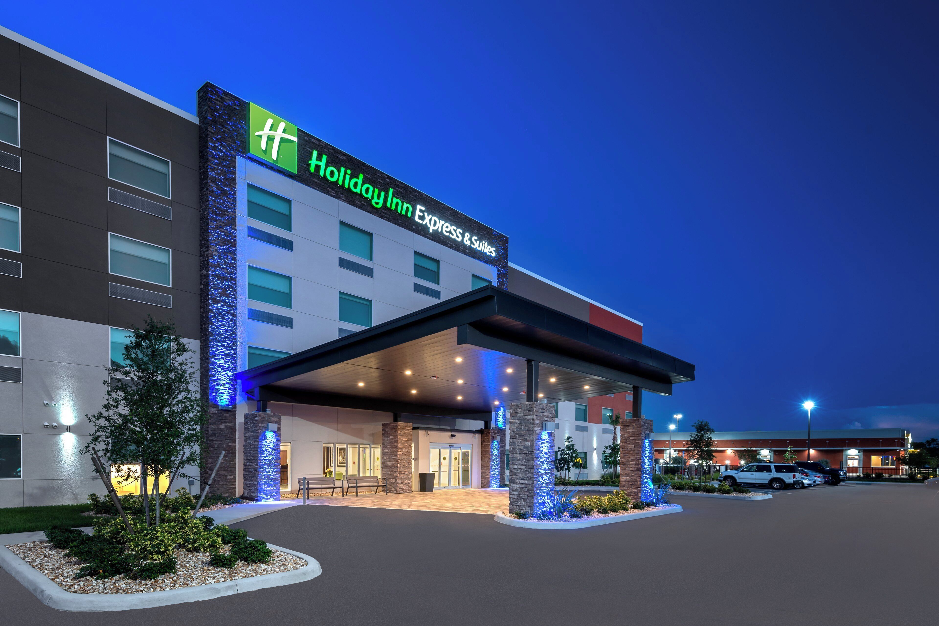 Un bâtiment de la chaîne Holiday Inn Express & Suites, doté d’une façade moderne, de grandes fenêtres et d’un espace d’entrée abrité.