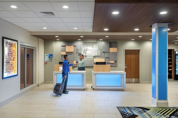 A hotel reception area with a modern design, including a reception desk, a digital display, and a framed artwork on the wall.