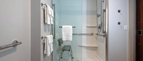 A glass-enclosed shower area with a chair, a towel rack, and a shower head.