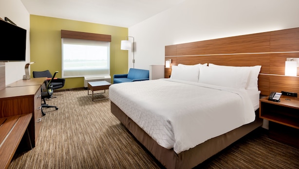 A hotel room with a large bed, a desk, a chair, a TV, and a window with a view.