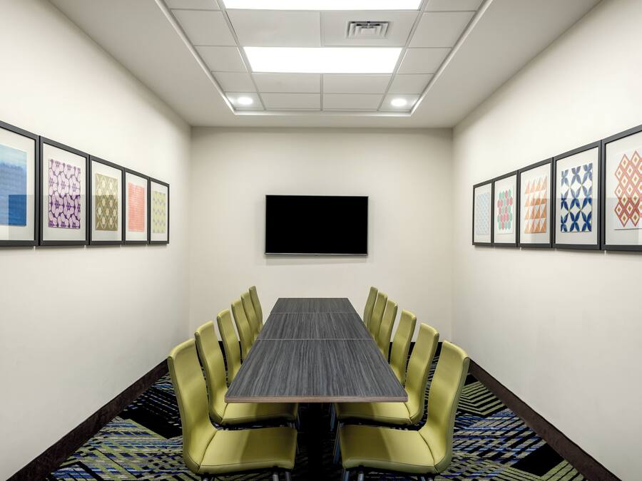 Un salón de conferencias con una larga mesa, sillas amarillas, obras de arte enmarcadas en las paredes y un televisor de pantalla plana montado en la pared.