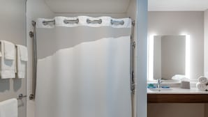 A bathroom with a shower curtain, a glass door, a sink with a mirror, and towels on the wall.