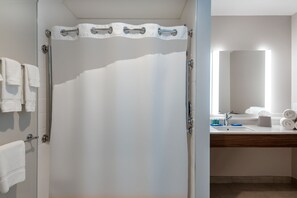 Een badkamer met douchegordijn, glazen deur, wastafel met spiegel en handdoeken aan de muur.