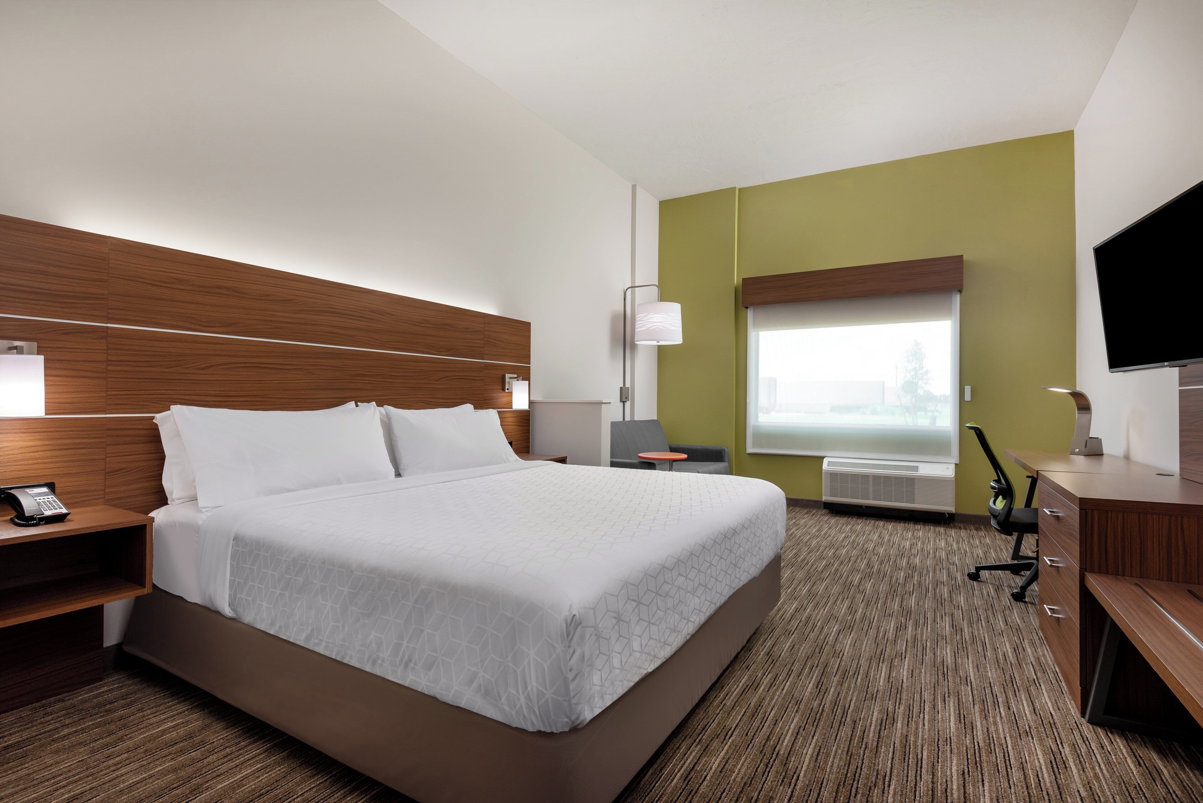 A hotel room with a large bed, a desk, a chair, a flat-screen TV, a telephone, and a window.