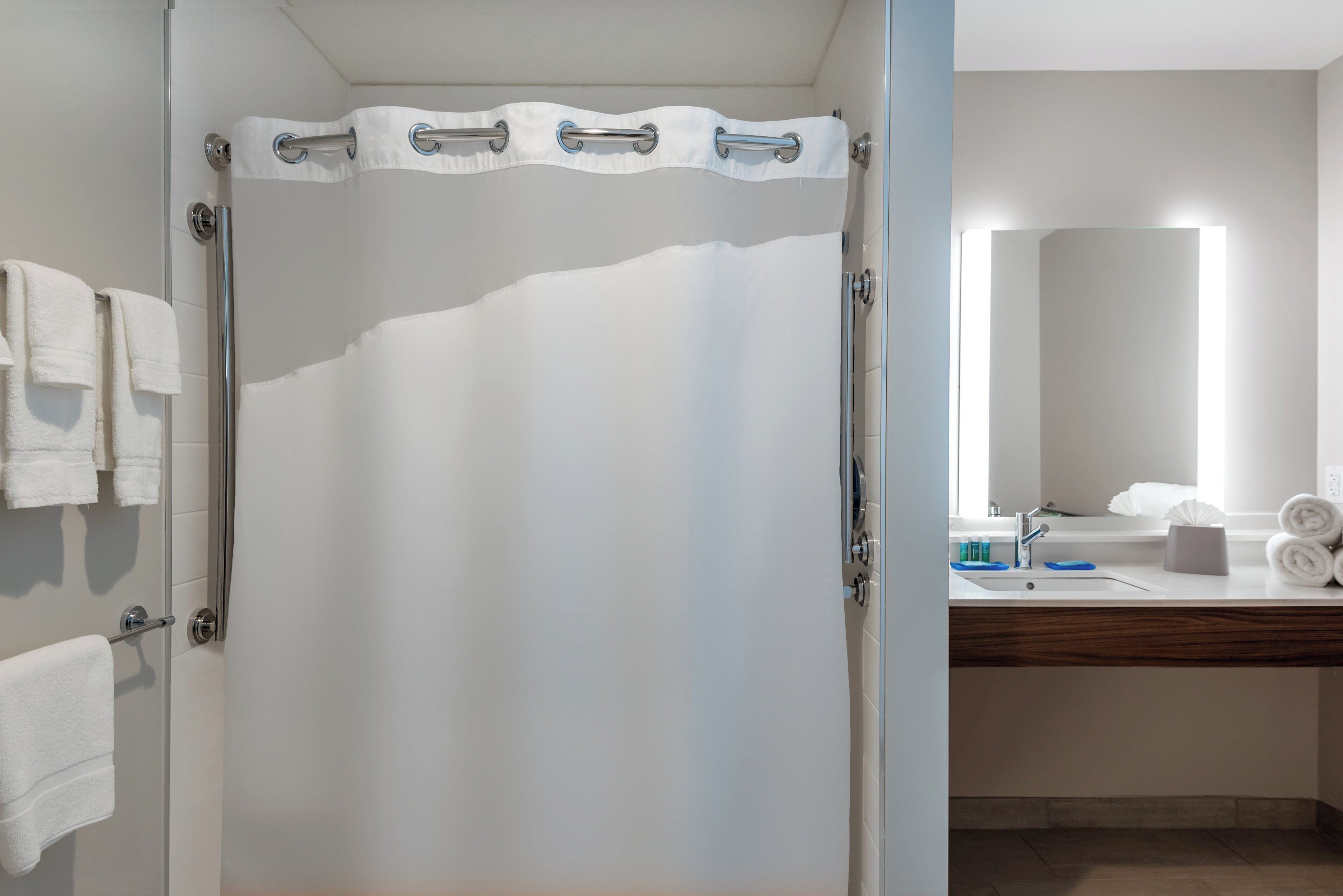 Un bagno con tenda doccia, un portasciugamani con asciugamani, un lavandino con articoli da toilette e uno specchio.