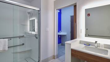A modern bathroom with a glass shower enclosure, a white sink with a wooden vanity, and a blue accent wall.