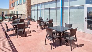An outdoor patio with tables and chairs, a pool in the background, and a building with large windows. - Holiday Inn Express & Suites El Paso East-Loop 375 by IHG (El Paso)