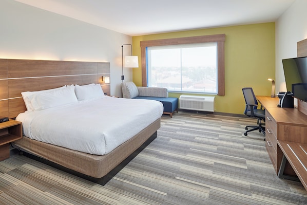 Quarto de hotel com uma cama grande, uma escrivaninha com computador, uma cadeira e uma televisão.