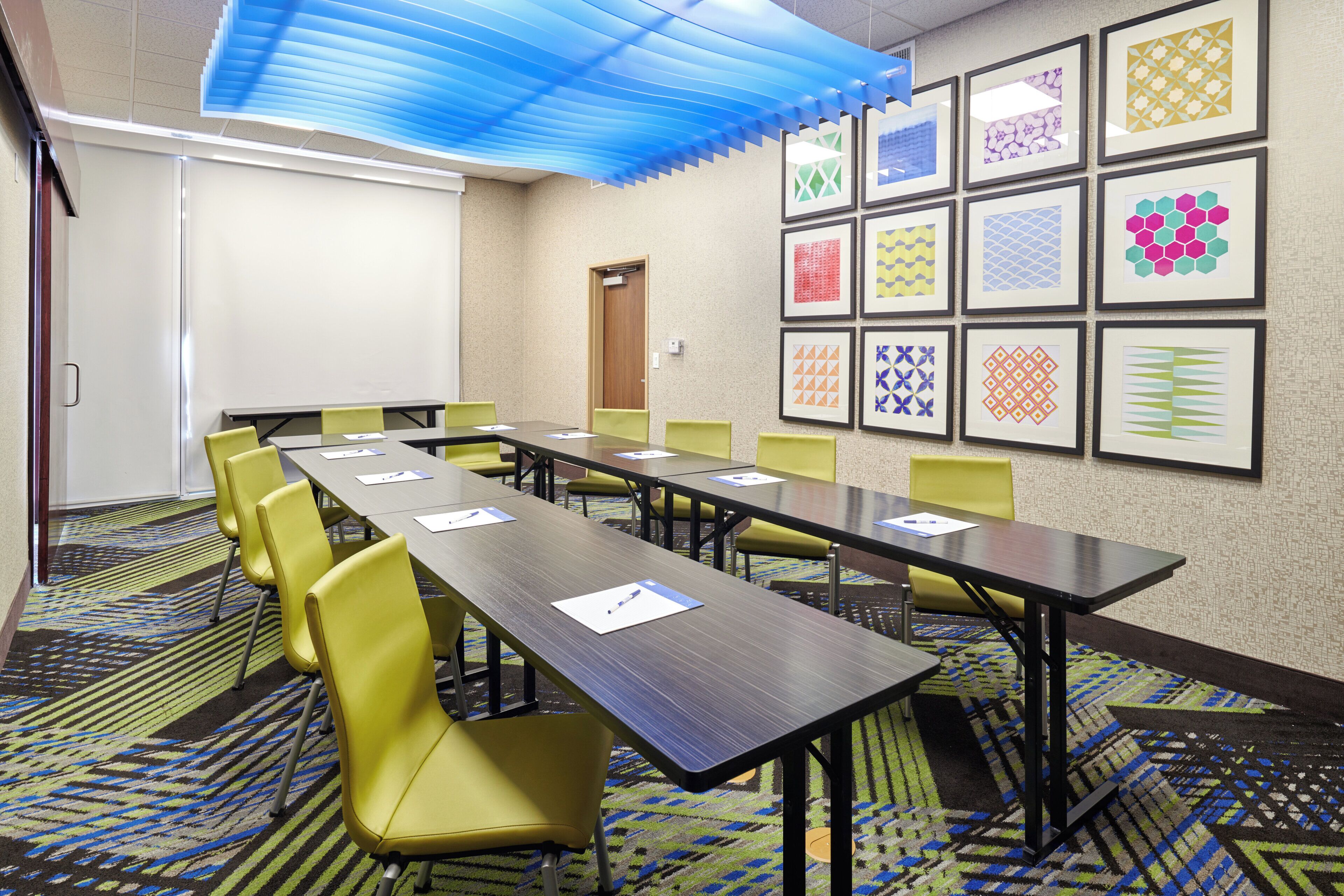 A conference room with a long table, yellow chairs, and framed geometric patterns on the walls.