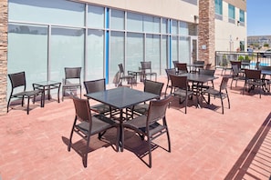 An outdoor patio with tables and chairs, large windows, and a stone wall. - Holiday Inn Express & Suites El Paso East-Loop 375 by IHG (El Paso)