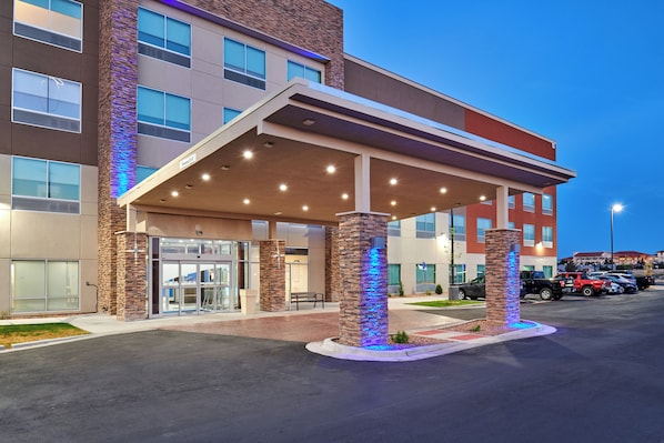 A hotel entrance with a covered waiting area, a glass door entrance, and a parking lot with vehicles. - Holiday Inn Express & Suites El Paso East-Loop 375 by IHG (El Paso)