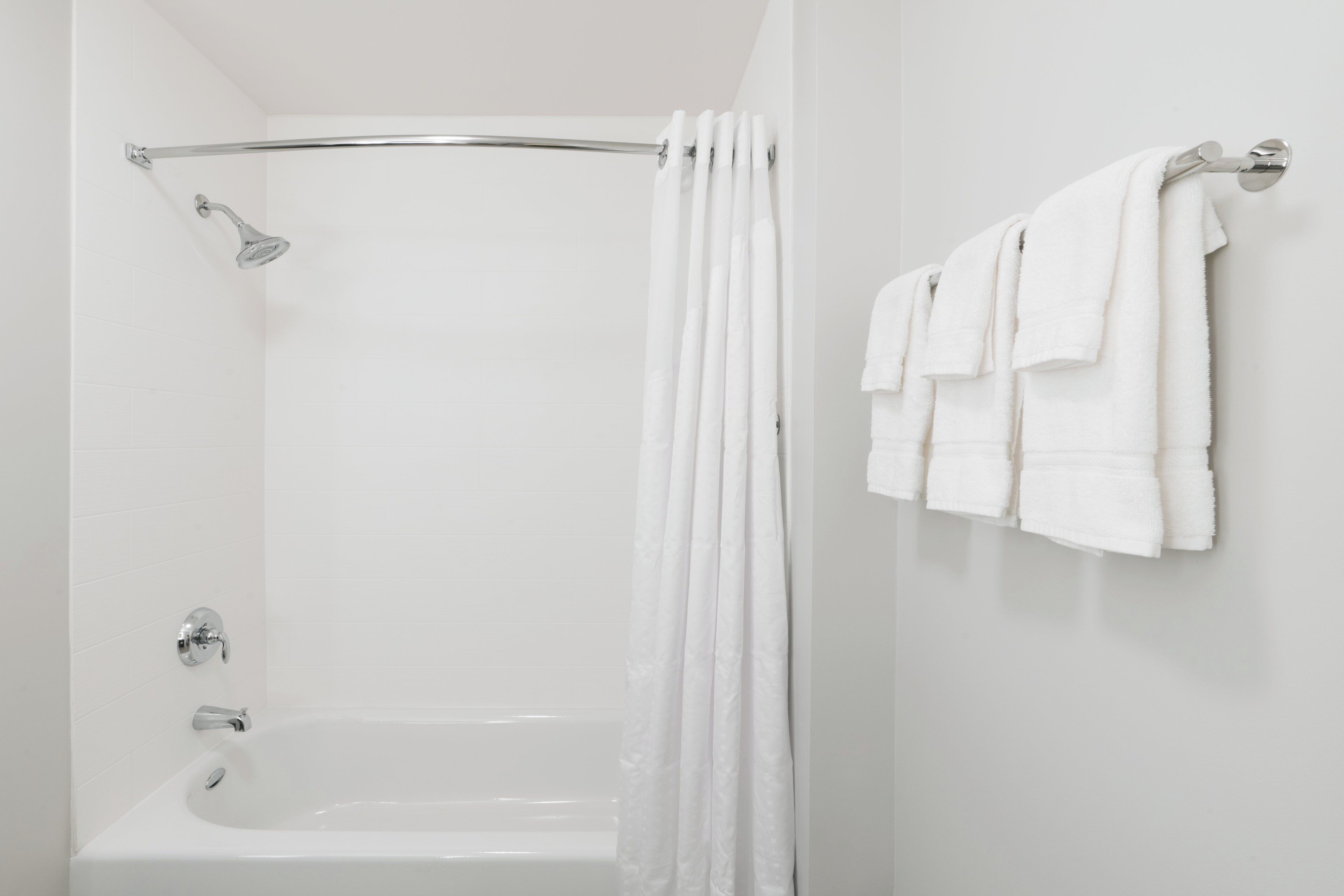 Une salle de bain avec une baignoire blanche, une pomme de douche et un porte-serviettes avec plusieurs serviettes.