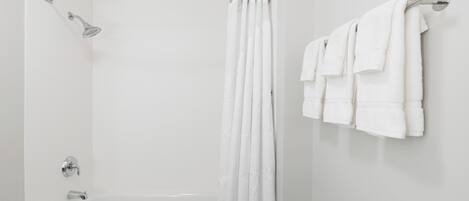 Baño con una bañera blanca, cabezal de ducha y toallero con varias toallas.