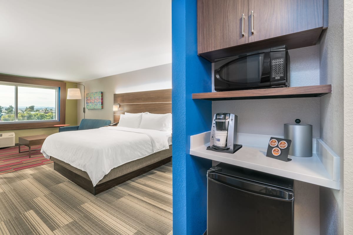 Une chambre d’hôtel équipée d’un lit, d’un bureau avec une machine à café, d’un four à micro-ondes et d’un petit réfrigérateur.