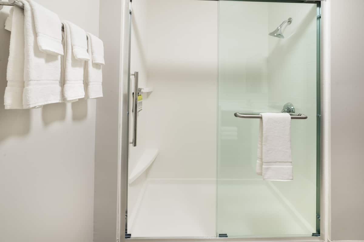Une salle de bain moderne avec une douche à parois de verre, une baignoire blanche et un porte-serviettes muni de plusieurs serviettes.