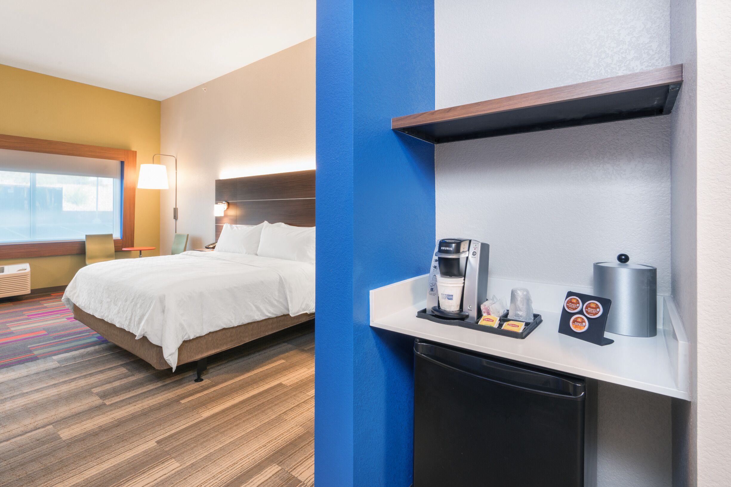 Ein Hotelzimmer mit Bett, Schreibtisch mit Kaffeemaschine und kleinem Kühlschrank.