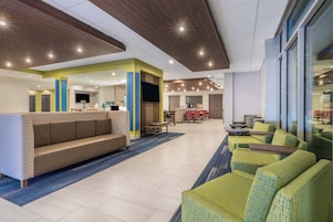 A modern hotel lobby with a seating area, a reception desk, and a dining area.
