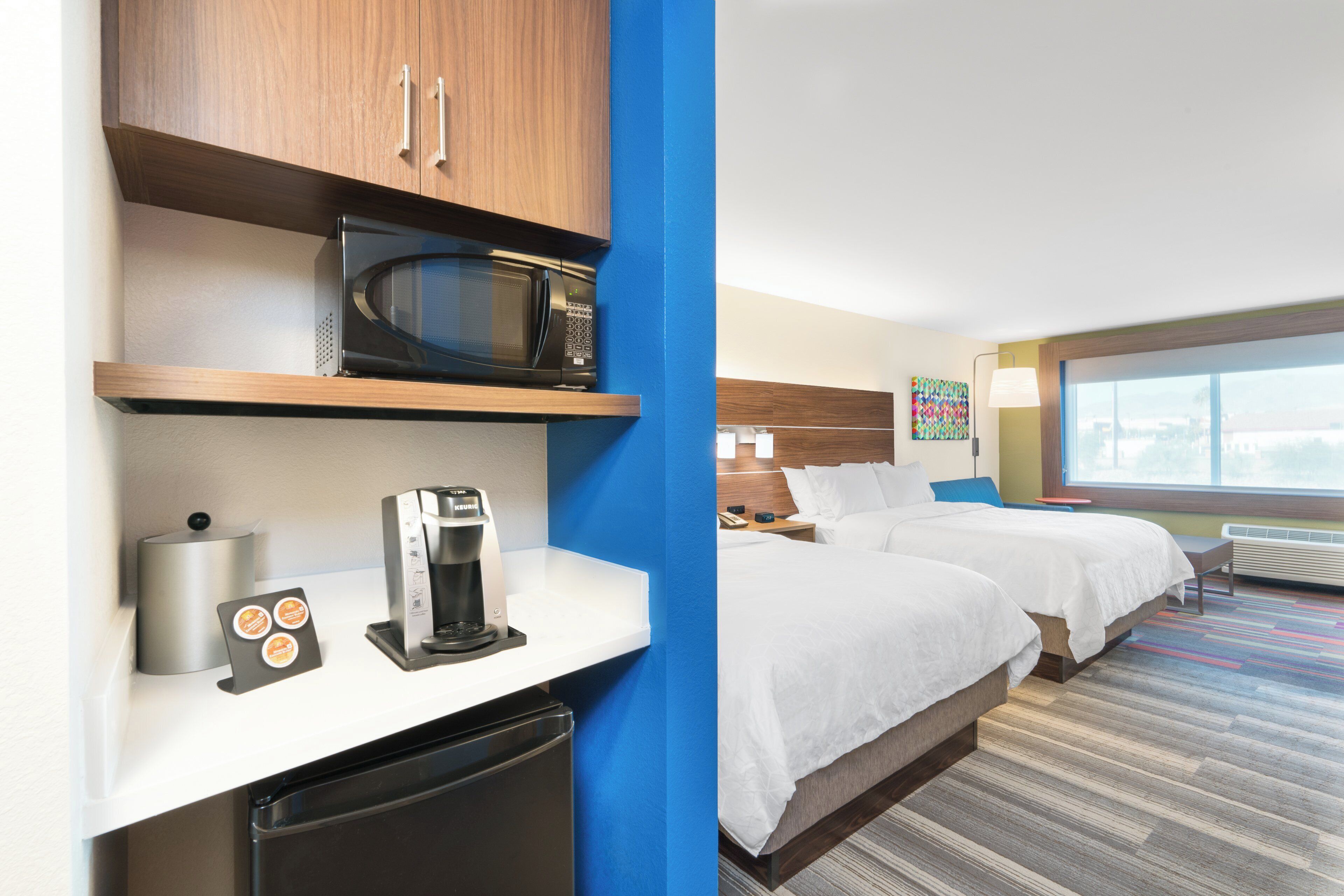 Een hotelkamer met een kitchenette, een bed, een nachtkastje en een raam.