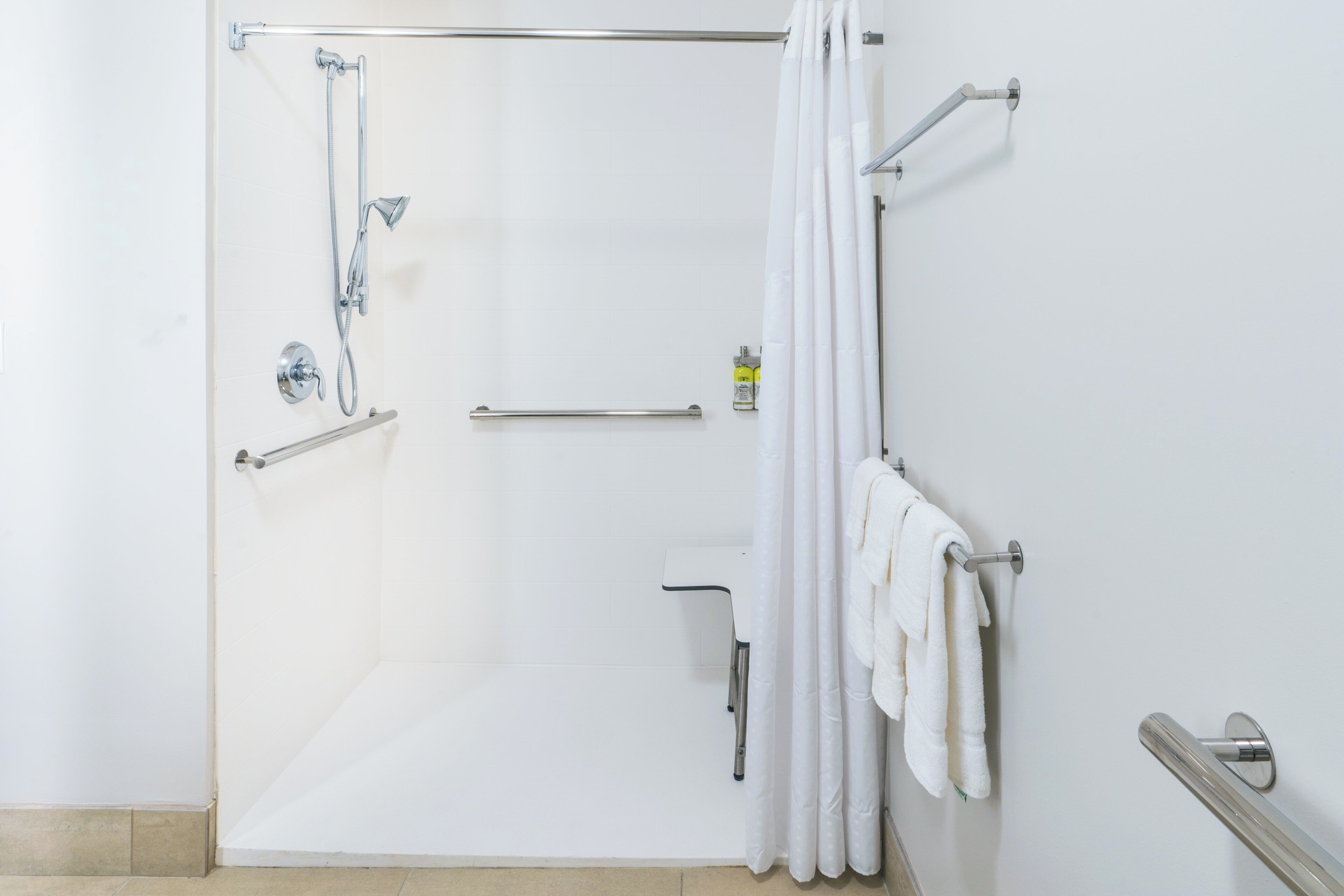 A shower area with a glass door, a handrail, a towel rack, and a grab bar.