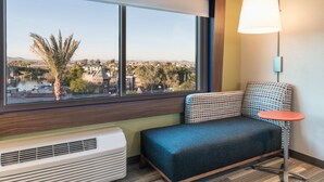 Ein Hotelzimmer mit großem Fenster, einer Couch, einem kleinen Tisch und einer Wandlampe.