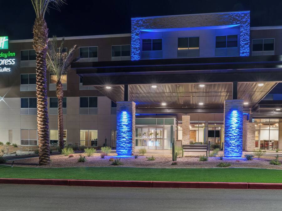 Edifici d'Holiday Inn Express & Suites amb façana moderna, detalls blaus il·luminats i zona exterior ben cuidada amb palmeres i vorera vermella.