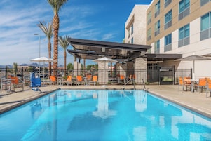 A swimming pool with lounge chairs and umbrellas, surrounded by a fence and palm trees.
