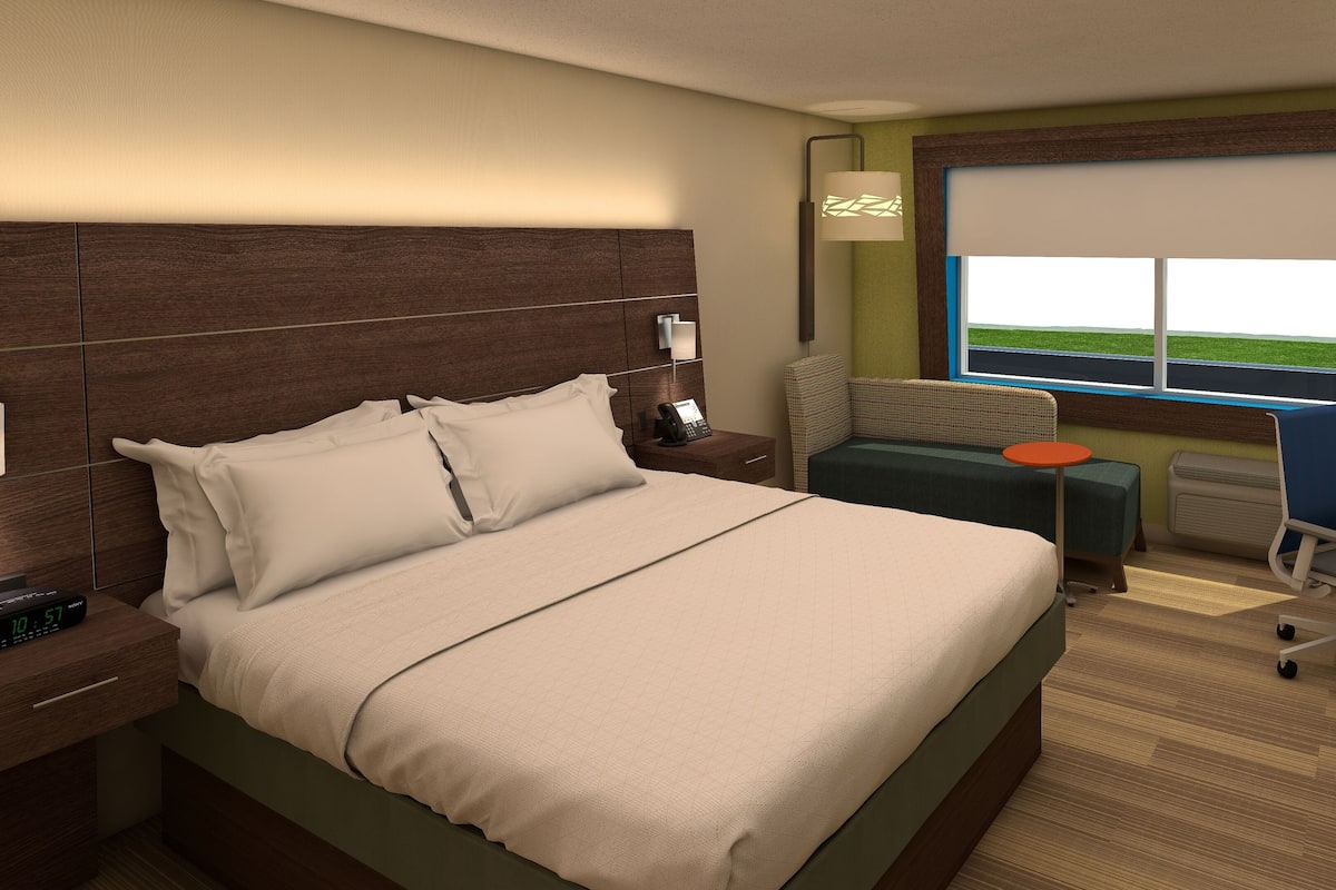 Une chambre d’hôtel avec un grand lit, une table de chevet, une lampe, une fenêtre avec vue et un bureau avec une chaise.