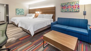 Ein Hotelzimmer mit einem großen Bett, einem blauen Sofa, einem Holztisch und einem farbenfrohen, abstrakten Gemälde an der Wand.