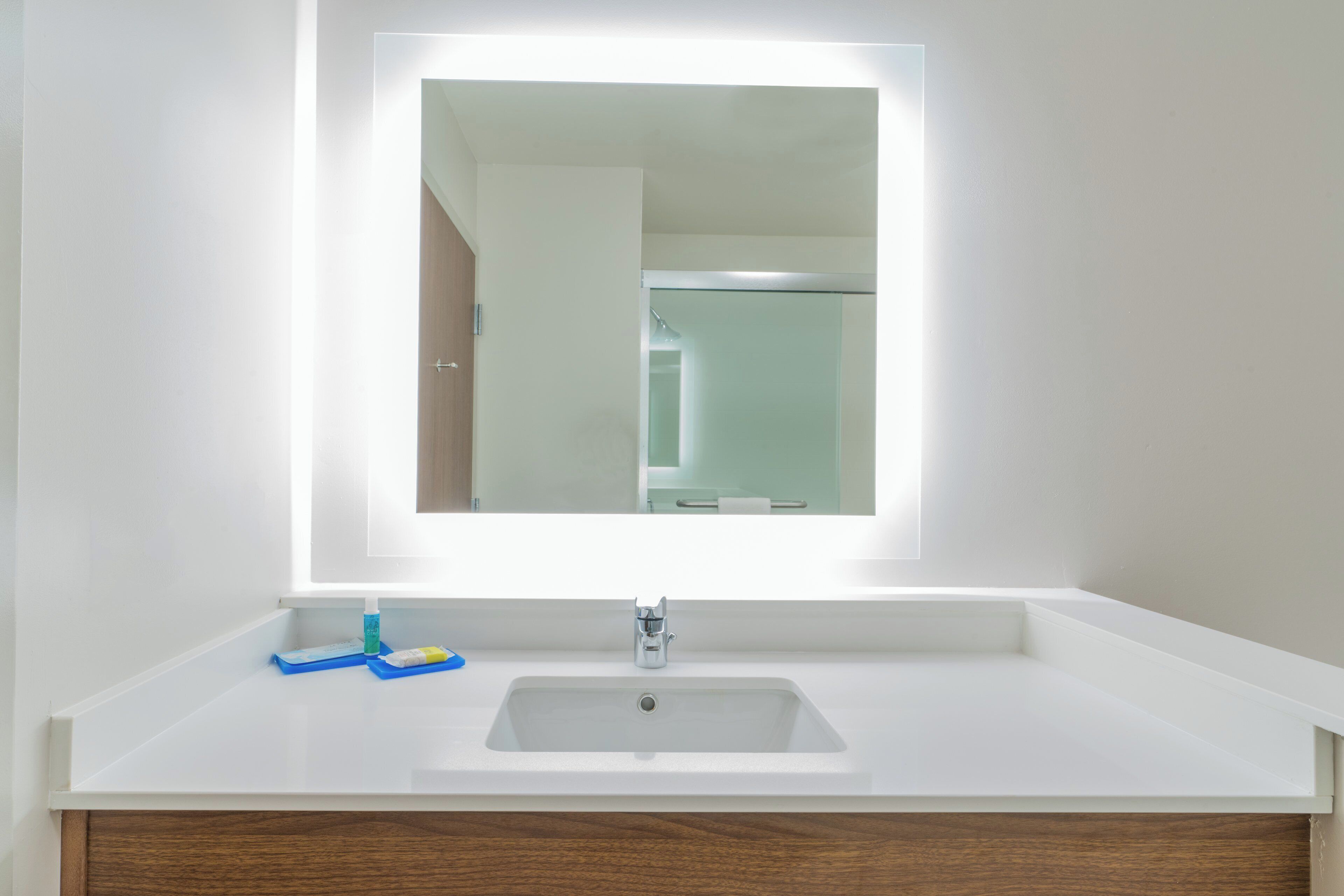 Un baño con un lavabo blanco, un espejo y un mueble de tocador de madera.