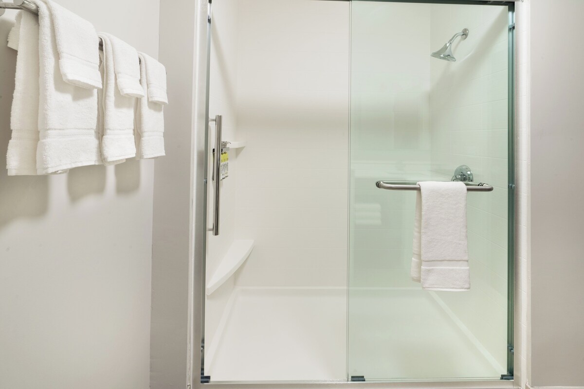 Une douche fermée par des parois de verre, avec une serviette blanche accrochée au mur.