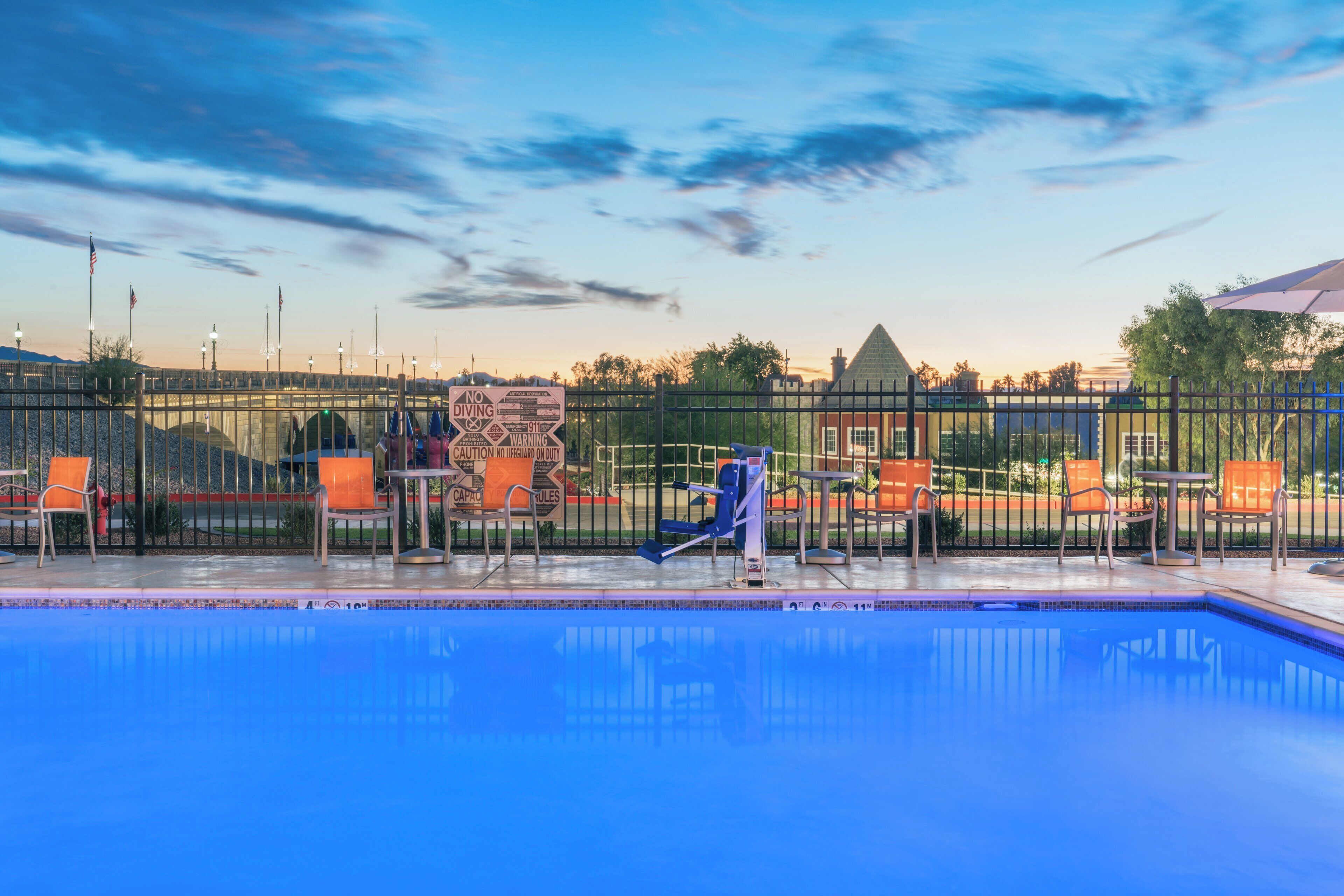 Piscina com trampolim, rodeada por cadeiras e uma cerca com placas de aviso.