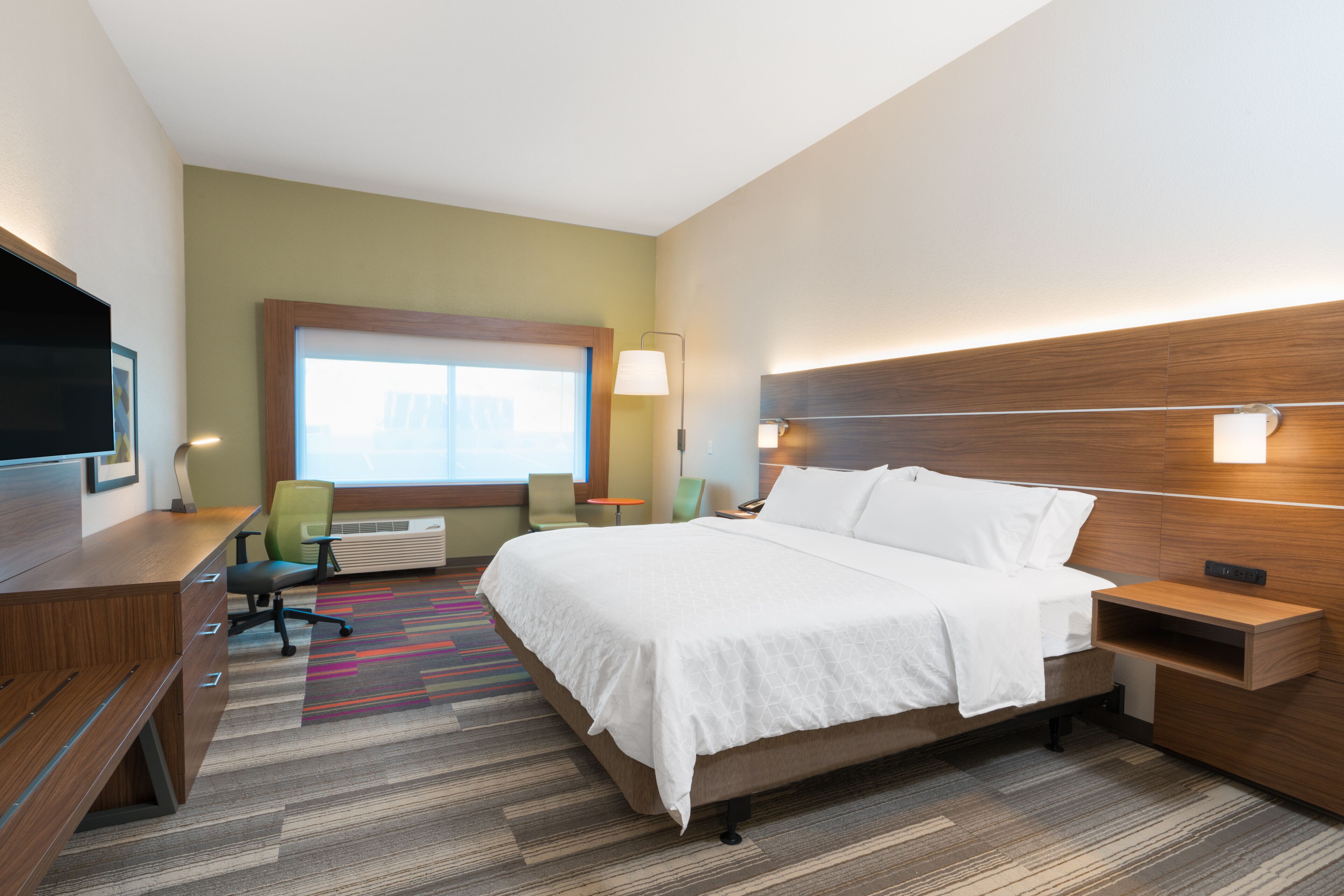 A hotel room with a bed, desk, chair, and a TV.