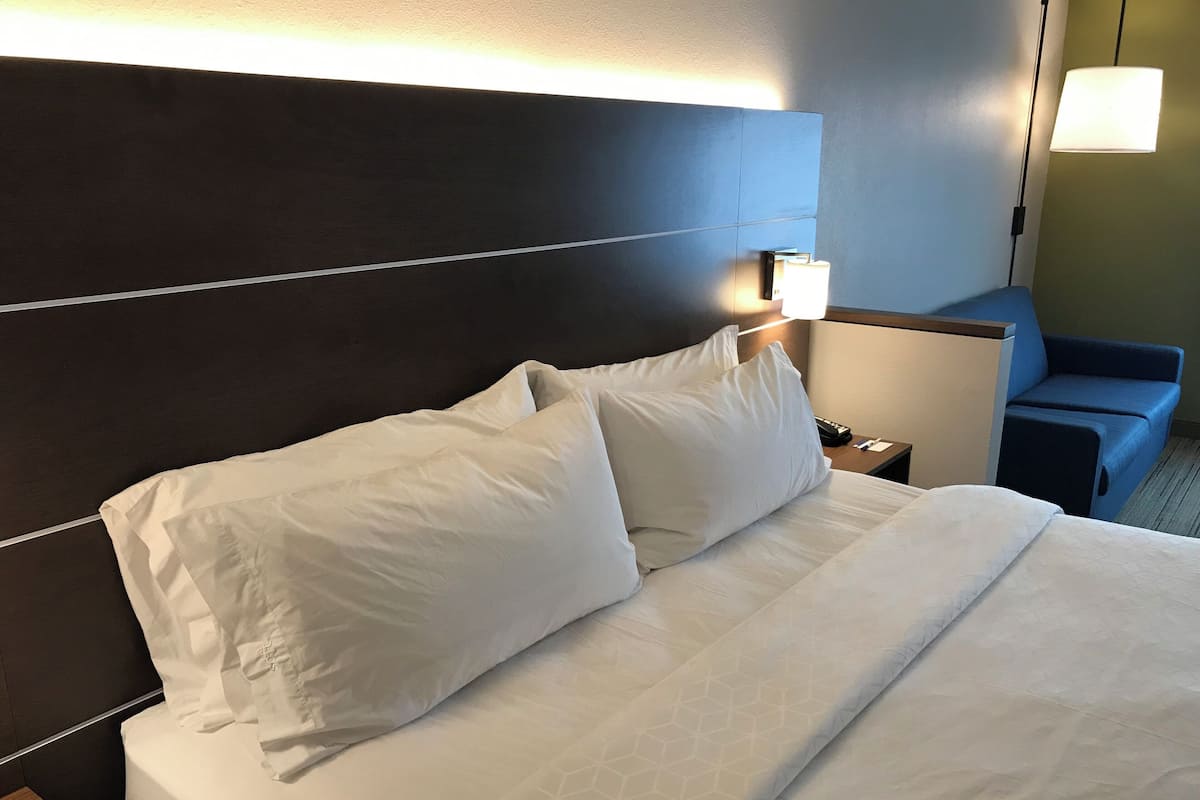 Ett hotellrum med en väl bäddad säng, en sänglampa, ett nattduksbord och en blå fåtölj.
