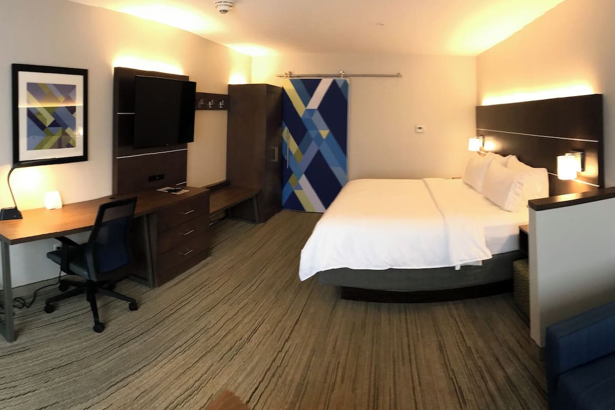 Ett hotellrum med en säng, ett skrivbord med en stol, en tv, ett nattduksbord och en lampa.