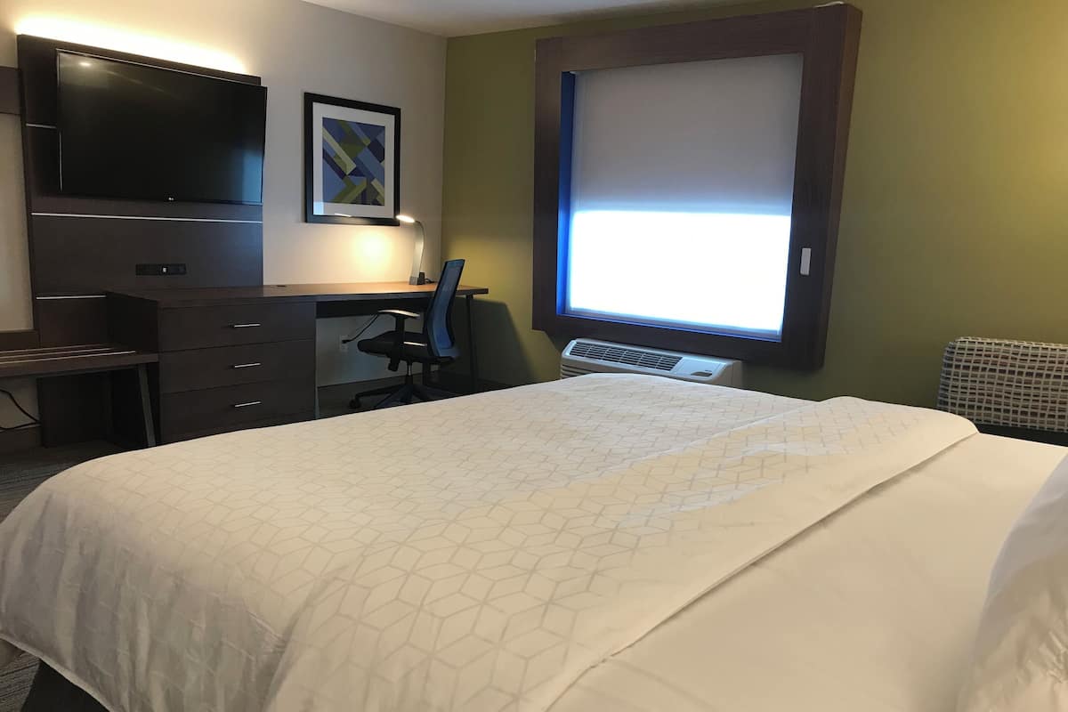 Ett hotellrum med en säng, ett skrivbord, en stol, en platt-TV och ett fönster med persienner.