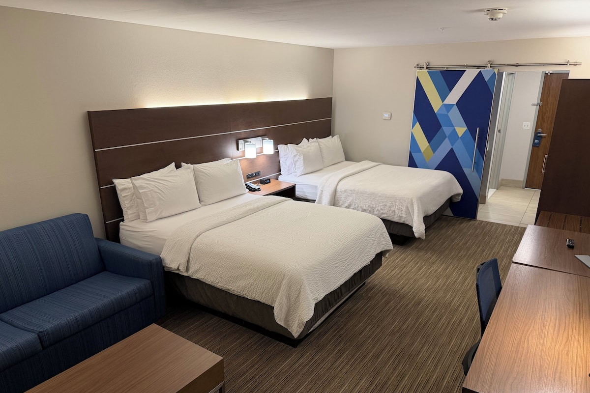 Ett hotellrum med två sängar, en blå soffa, ett träbord och ett skrivbord.