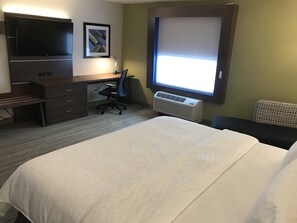 A hotel room with a bed, a desk with a chair, a flat-screen TV, an air conditioner, and a window with blinds. - Holiday Inn Express & Suites Hannibal - Medical Center by IHG (Hannibal)