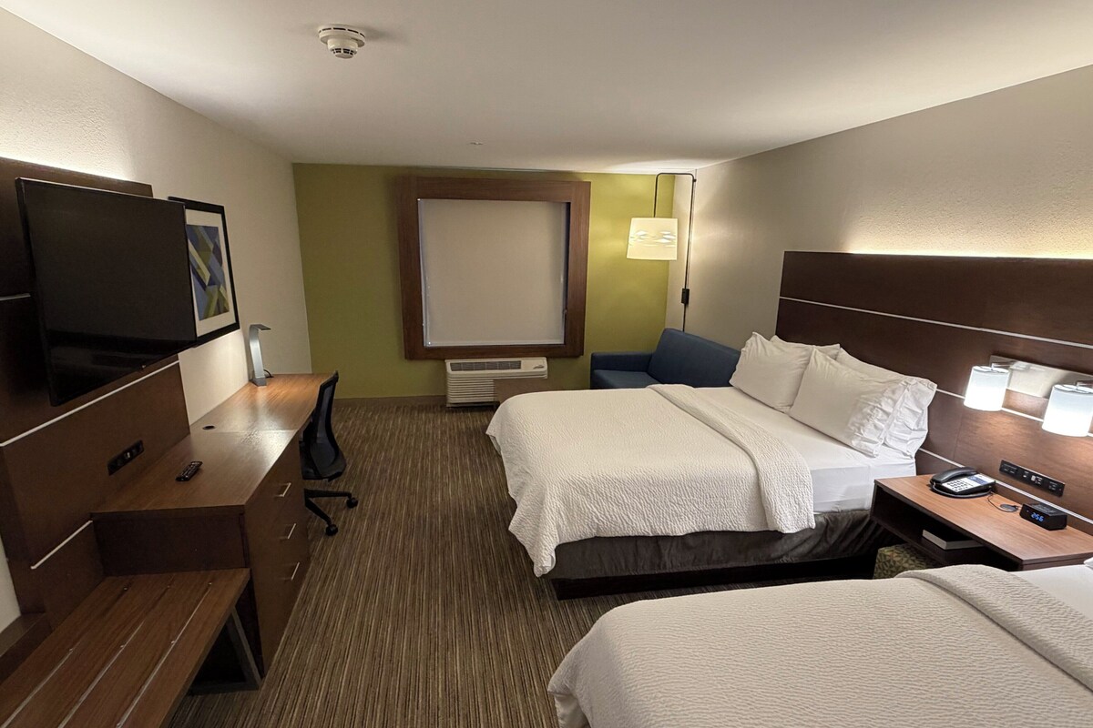 A hotel room with two beds, a desk with a TV, a chair, a bedside table with a phone, and a lamp.
