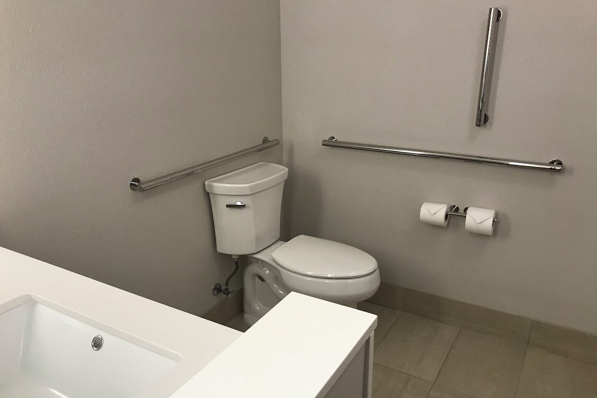 A bathroom with a white toilet, a grab bar, a roll of toilet paper, and a bathtub.