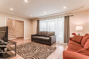 A living room with a sofa, a TV, a zebra-patterned rug, and a staircase.
